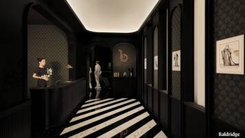 A hallway with a black and white striped floor, a reception desk, framed artwork on the walls, and a neon 'b' sign.
