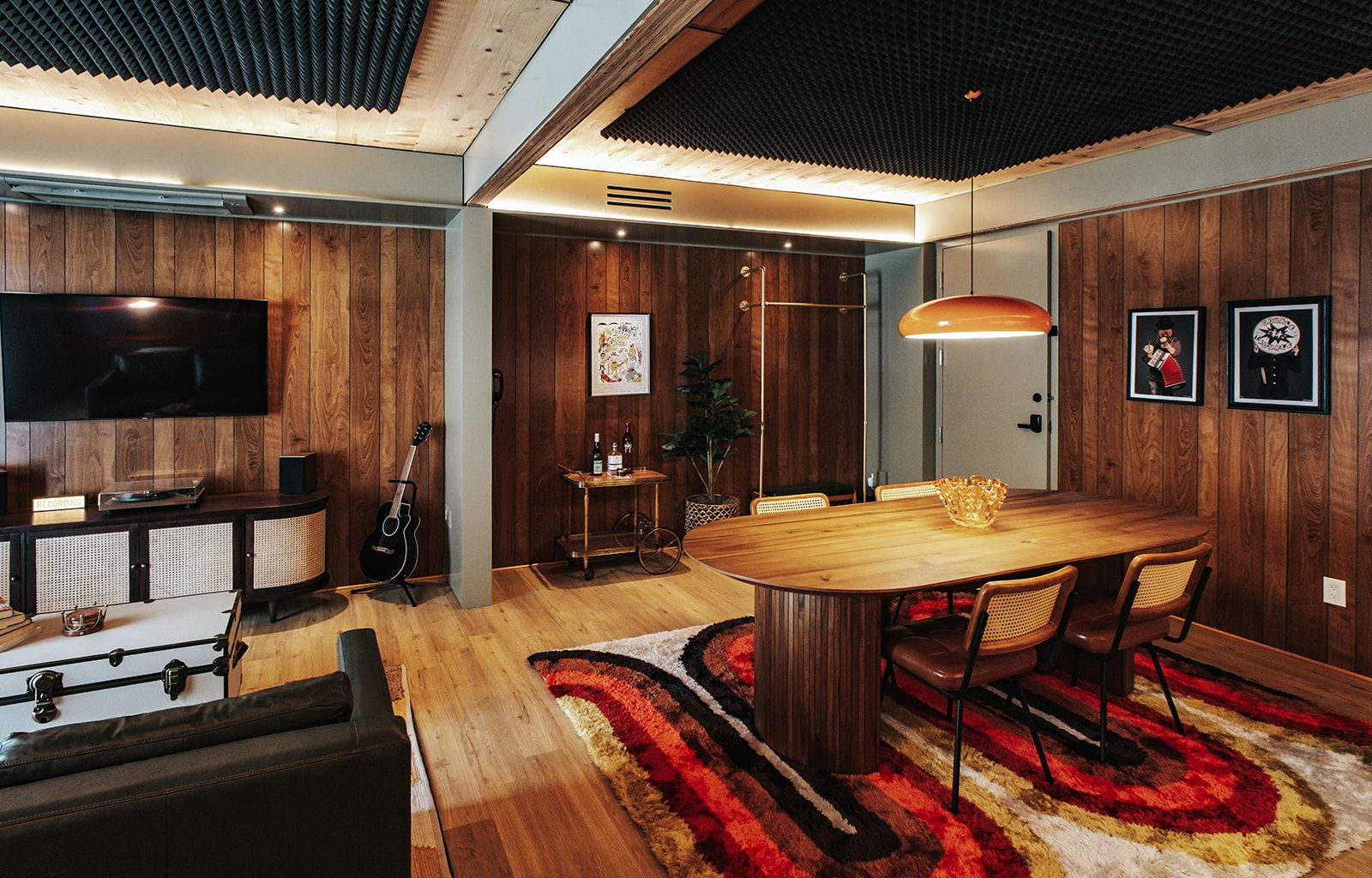 A modern living room with a wooden dining table, a television, and a guitar.
