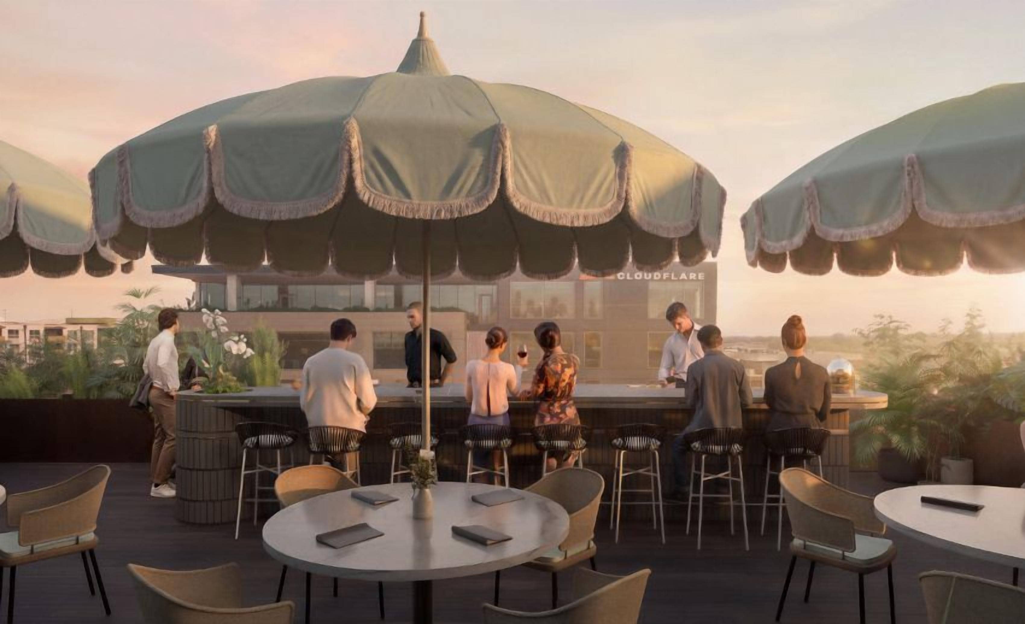 A rooftop bar with round tables and chairs, umbrellas, and a bar area with people.