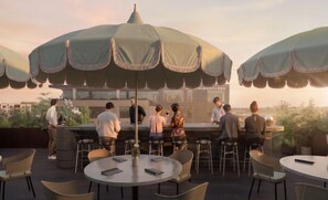 A rooftop bar with round tables and chairs, umbrellas, and a bar area with people.