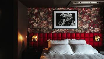 A bedroom with a red upholstered headboard, a framed black and white photograph, and two wall sconces.
