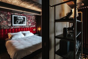 Una habitación de hotel con un cabecero tapizado en rojo, una fotografía blanco y negro enmarcada y un escritorio con lámpara.