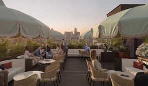 An outdoor seating area with tables and chairs, covered by large umbrellas, and a city skyline in the background. - bohème (Austin)