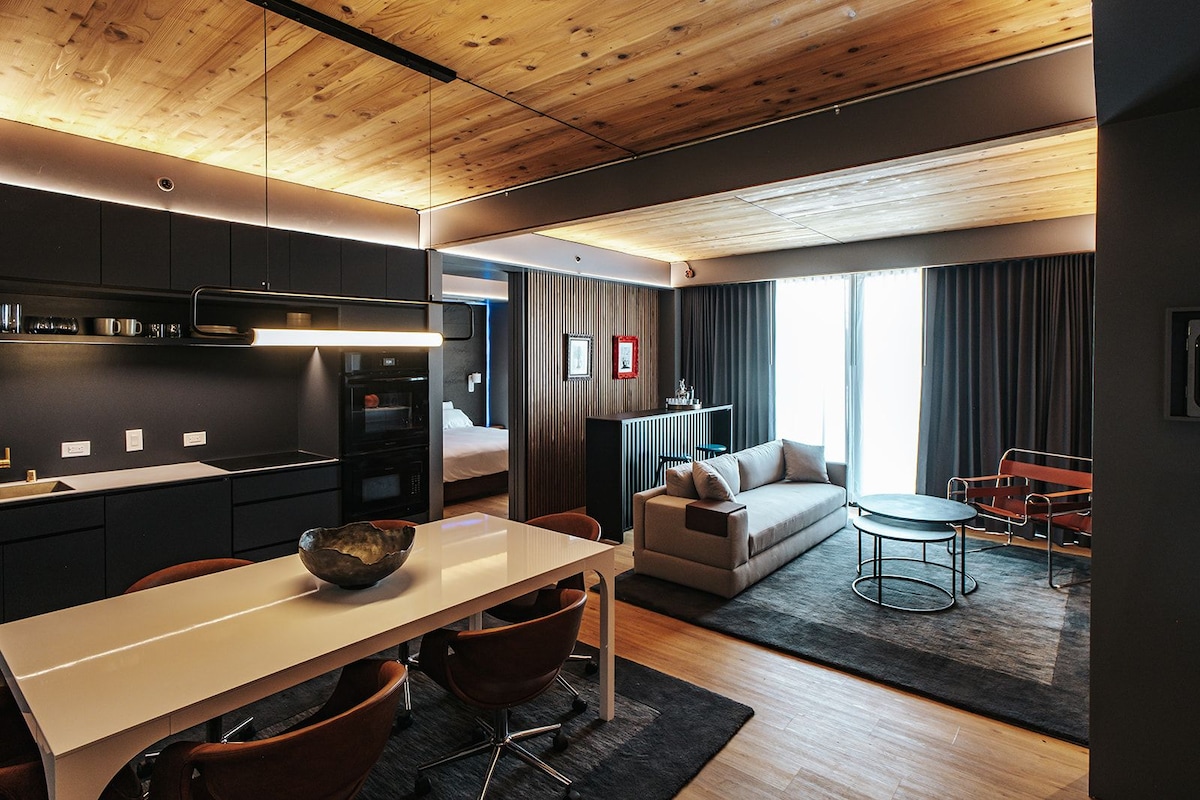 Una habitación de hotel moderna con kitchenette, comedor, sofá y una pequeña mesa redonda.