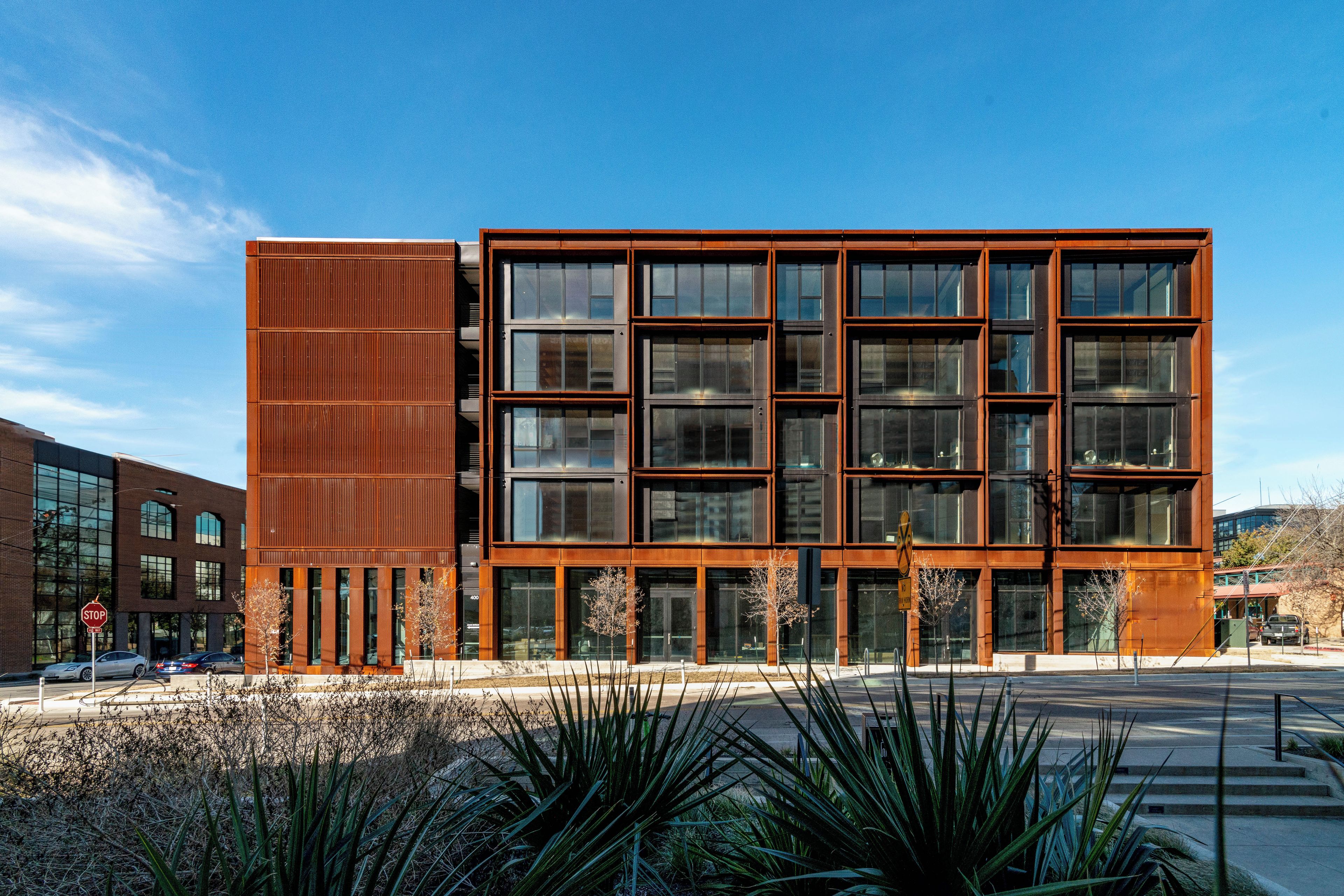 A modern building with a mix of glass and metal facade, featuring a prominent vertical metal panel on the left.
