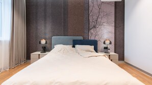 A neatly made bed with a headboard, two bedside lamps, a wall-mounted air conditioner, and a window with curtains. - Playwright Test Hotel 1789146053536 (Seattle)