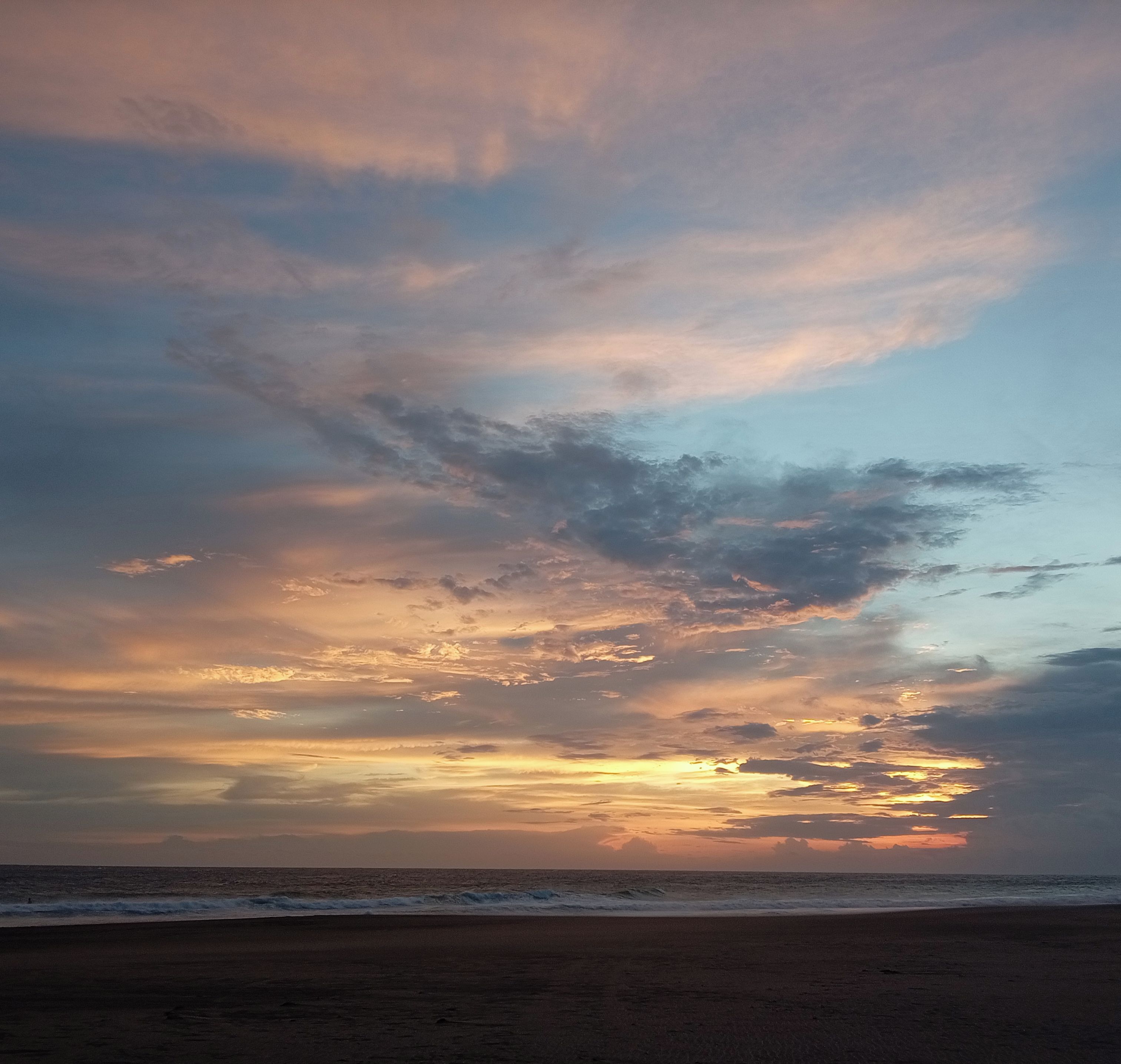 A beach with a sunset and clouds in the sky.