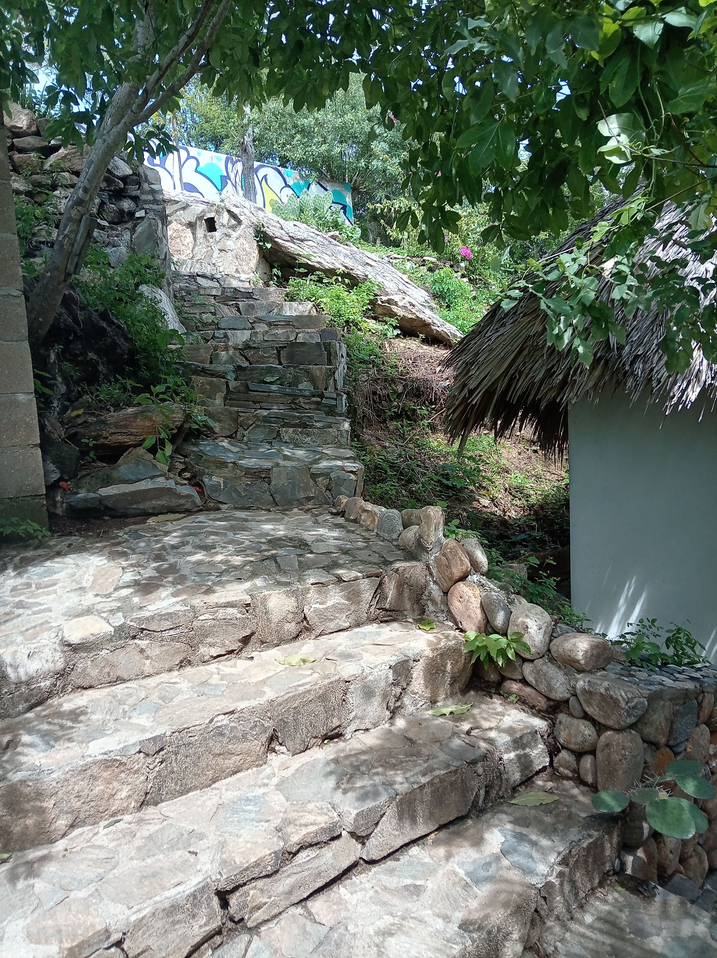 A stone staircase leading up to a stone wall with a mural, surrounded by greenery.