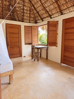 Ein Zimmer mit einem Strohdach, Holztüren, einem Tisch mit Stühlen und einem Bett.