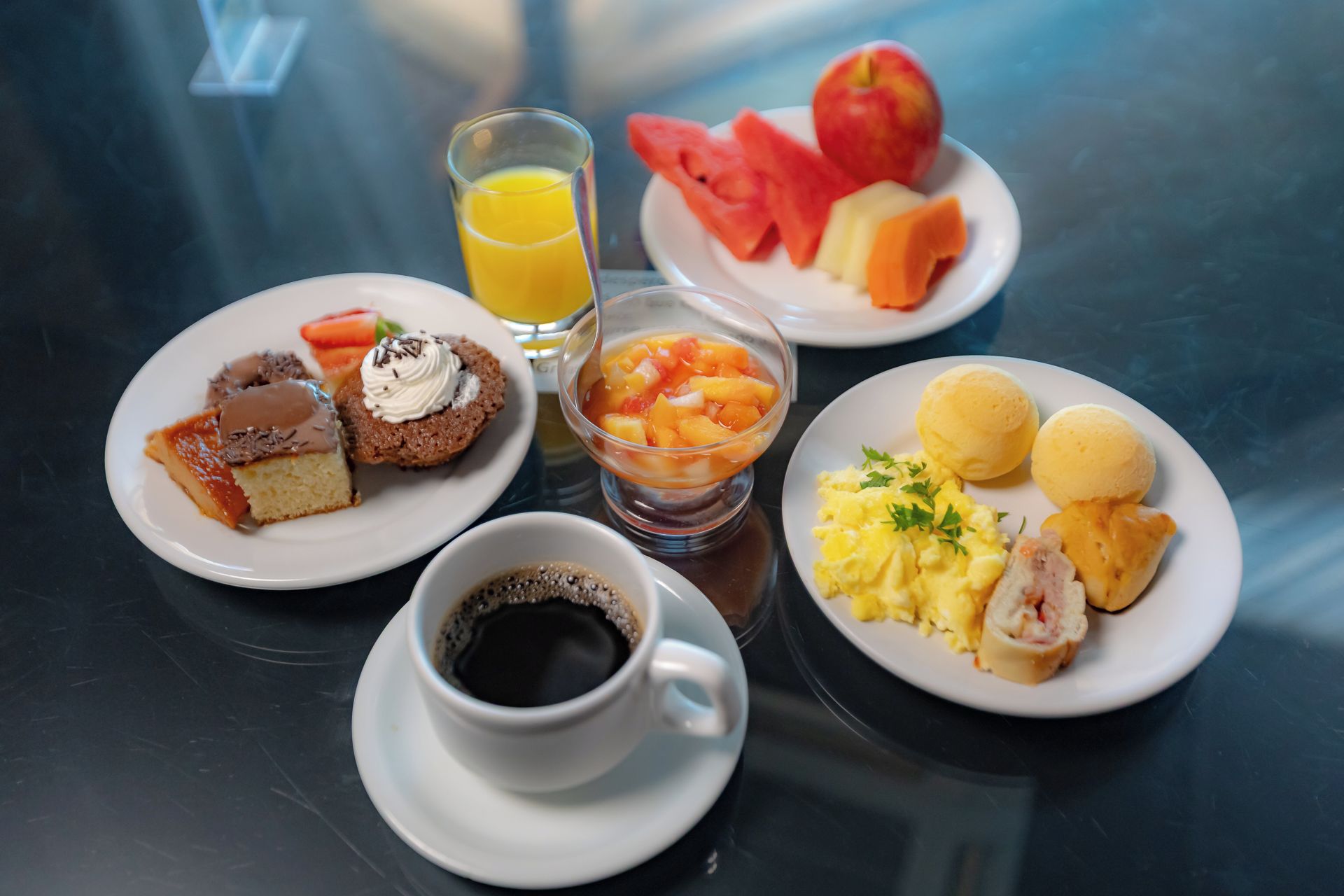 Un desayuno con platos de comida, un vaso de jugo de naranja y una taza de café.