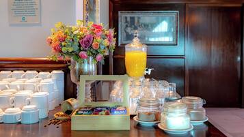 Montaje de un bufé de desayuno con tazas de café, un bol de frutas, un arreglo floral y un dispensador de jugo.