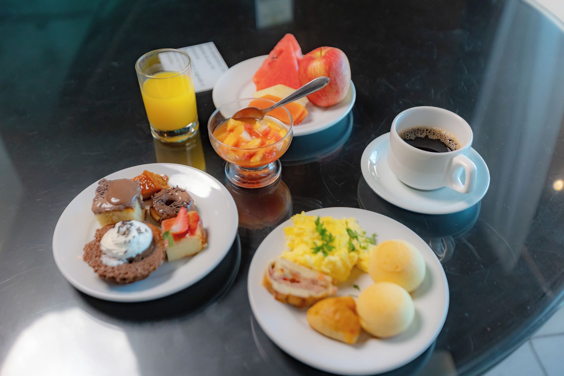 Une table de petit-déjeuner avec des assiettes remplies de nourriture, un verre de jus d’orange, un bol de fruits et une tasse de café.