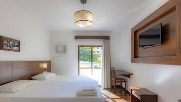 A hotel room with a bed, a desk, a television, and a window with curtains.