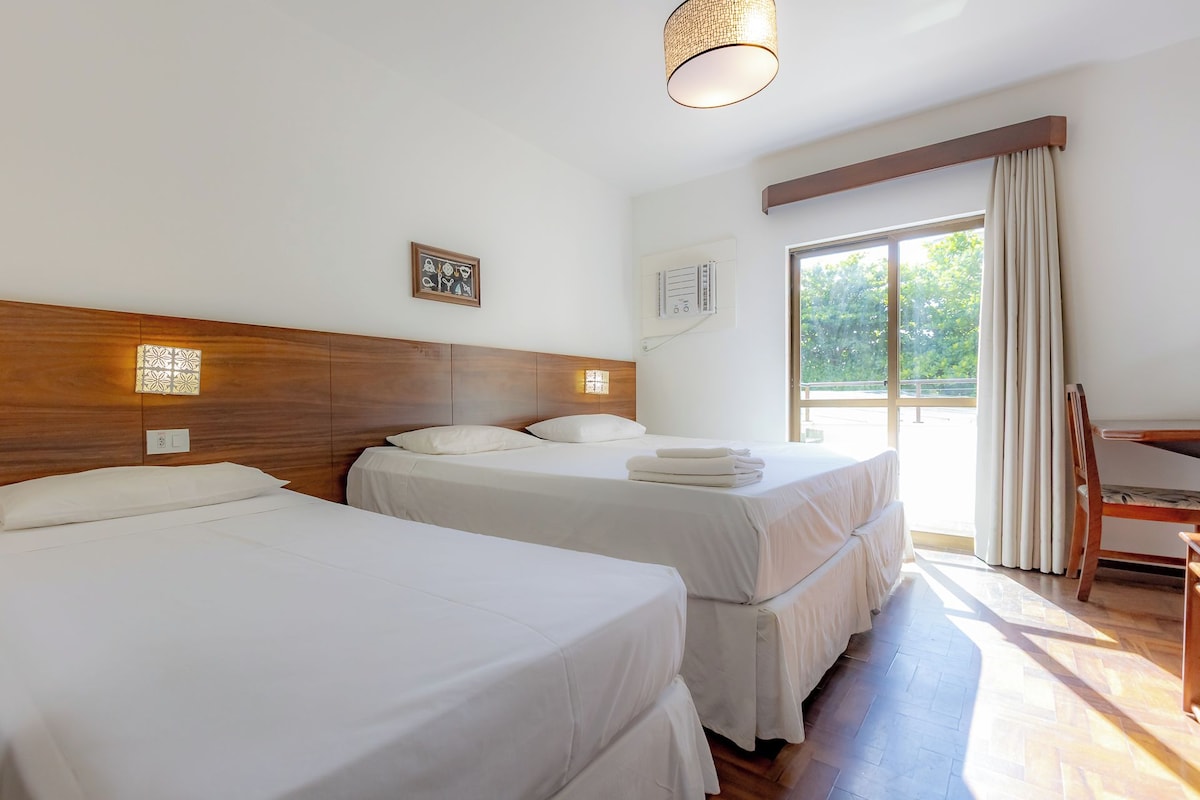 A hotel room with two beds, a wooden headboard, a window with curtains, and a desk.