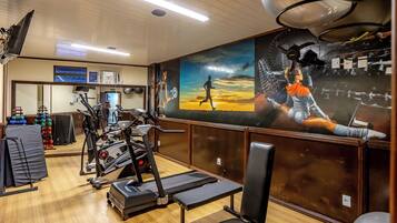 Un gimnasio con equipamiento de ejercicio, un mural y piso de madera.