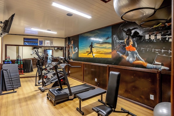 A gym with exercise equipment, a mural, and a wooden floor.