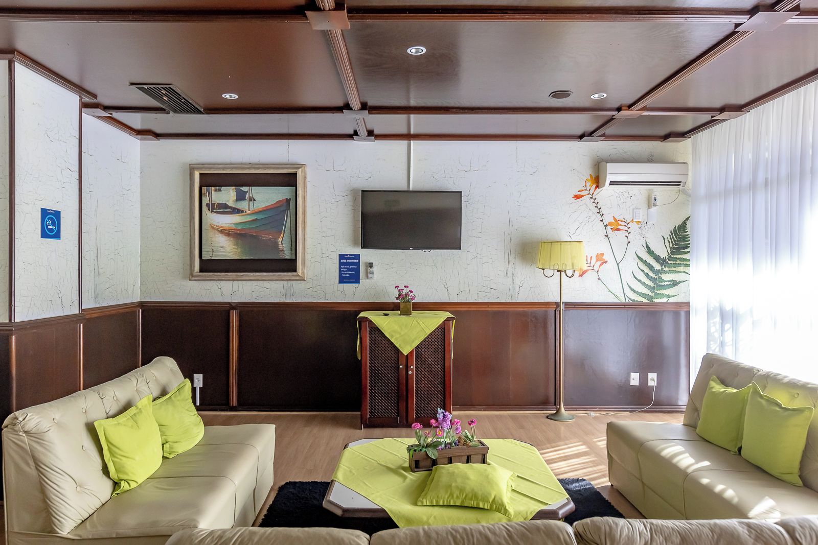 Un vestíbulo de hotel con una zona de estar, un televisor de pantalla plana, una planta decorativa y un equipo de aire acondicionado instalado en la pared.