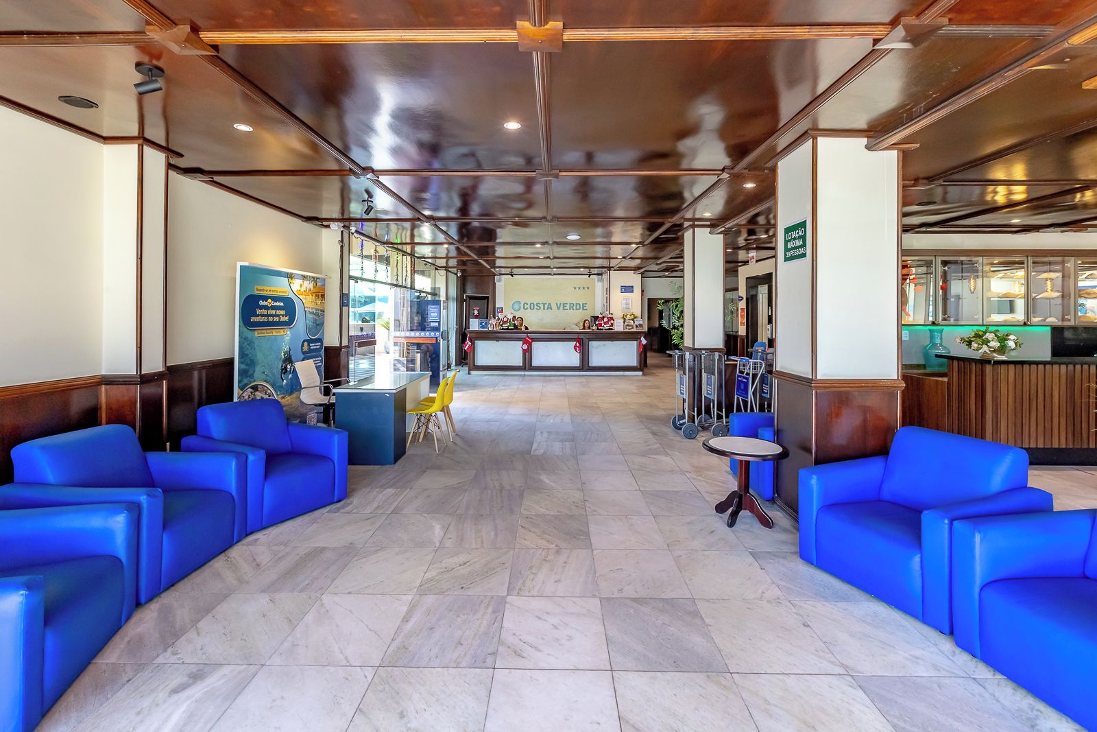 Un hall d'hôtel avec des sièges bleus, un comptoir d'accueil et un espace restaurant bien visible.