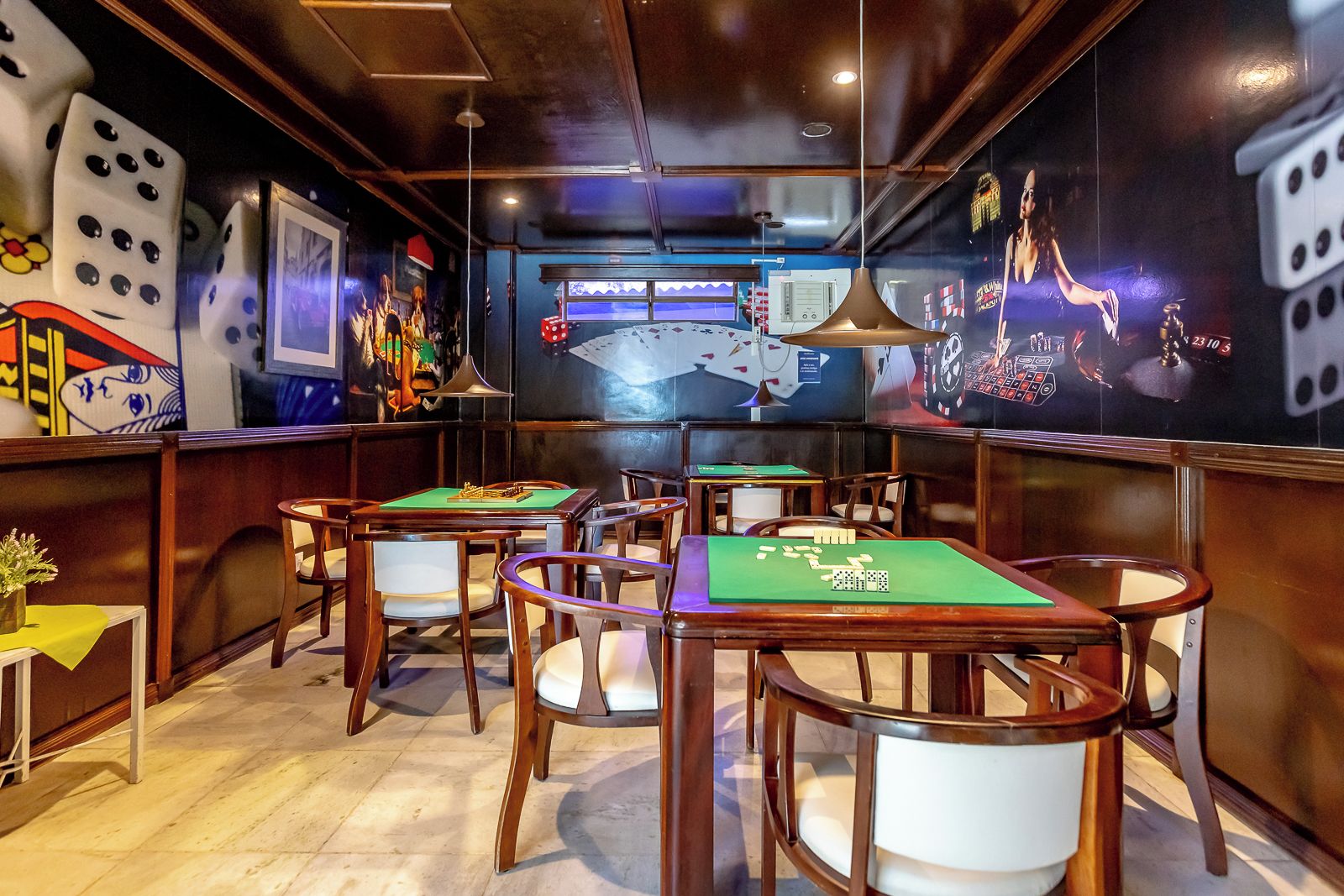 A room with multiple green felt tables and chairs, a clock on the wall, and dice-themed decorations.