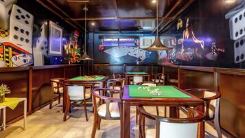 A room with multiple green felt tables and chairs, a clock on the wall, and dice-themed decorations.