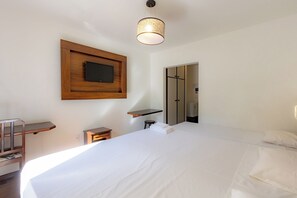 Habitación de hotel con cama, televisor montado en la pared, mesita de noche y espejo.
