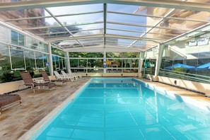 A clear glass-enclosed swimming pool with lounge chairs and a view of the outdoors. - Costa Verde By Candeias (Bombinhas)