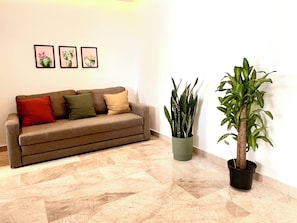 Ein Wohnzimmer mit einer Couch, Kissen, einer Topfpflanze und gerahmten Kunstwerken an der Wand.