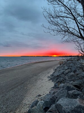 Uma praia com costa rochosa e um pôr do sol ao fundo.