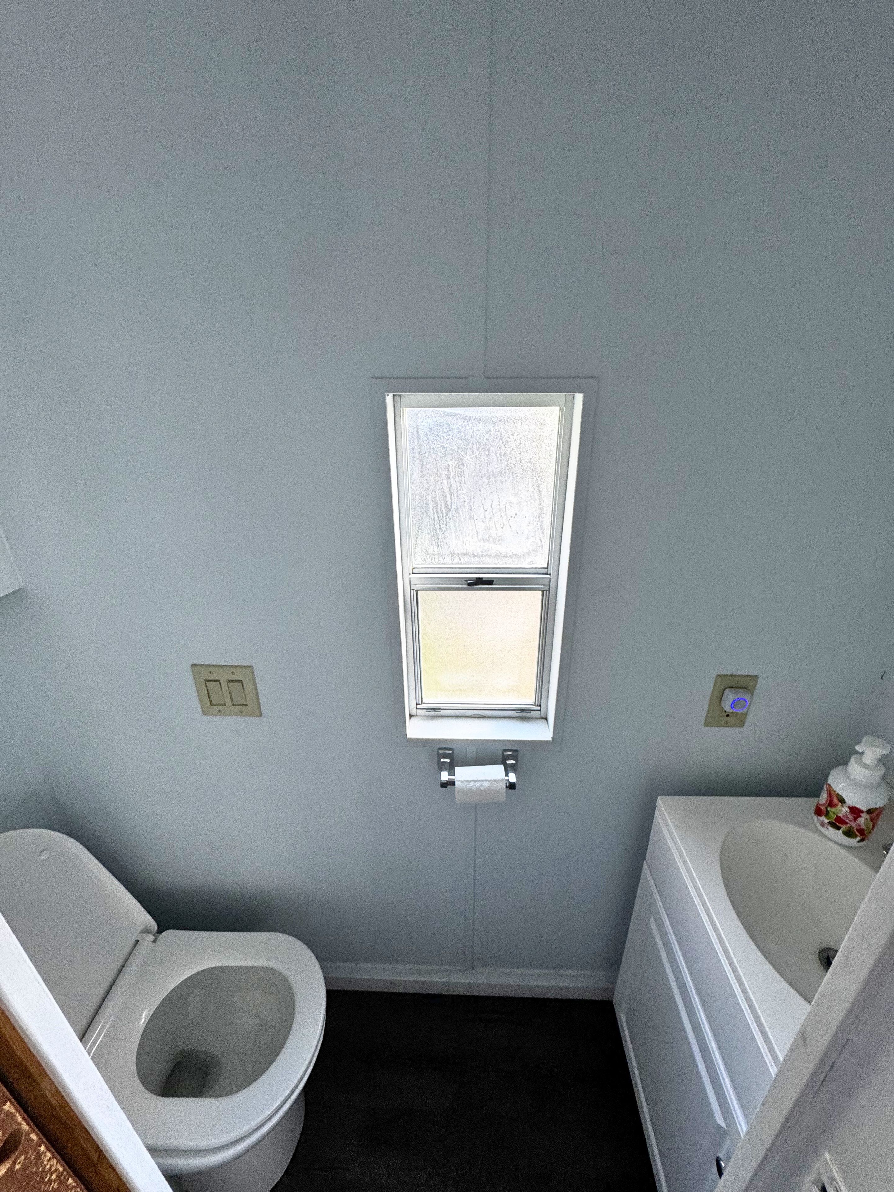 A small bathroom with a toilet, a window, and a sink.
