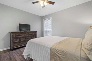 A bedroom with a bed, dresser, television, ceiling fan, and window with blinds. - Hamilton Harbor Hideaway | Lake Views & Pool (Hot Springs)
