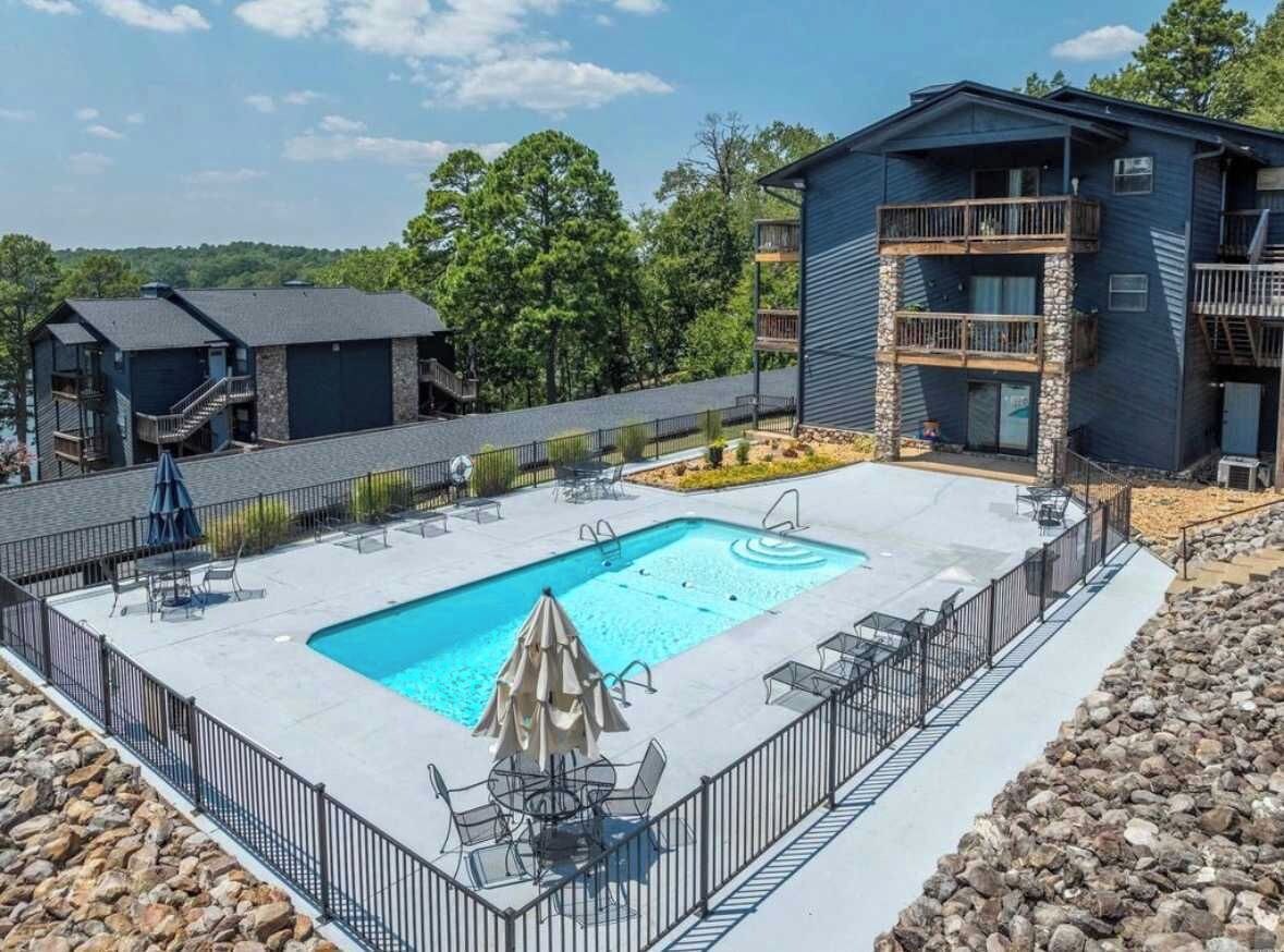A pool area with a rectangular pool, lounge chairs, and a building with balconies.