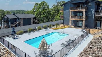 A pool area with a rectangular pool, lounge chairs, and a building with balconies.
