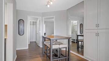 A modern kitchen with a wooden table and bar stools, a large mirror, and white cabinetry.