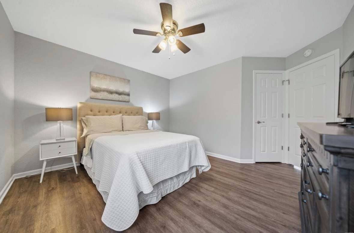 A bedroom with a bed, nightstand, ceiling fan, and a dresser.