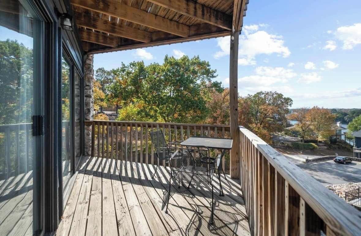 A wooden deck with a table and chairs, overlooking a residential area with trees and houses.