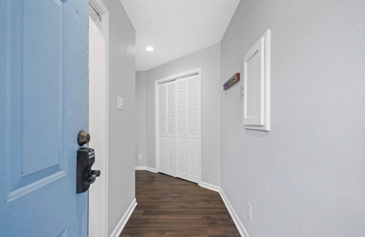 A hallway with a blue door, white closet doors, and a light switch on the wall.