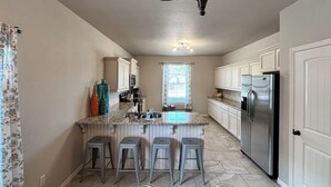 Una cocina con una isla central, taburetes de bar, un refrigerador y una ventana con cortinas.
