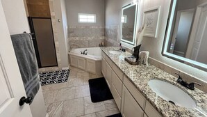 Un baño moderno con cabina de ducha, un mueble de tocador amplio con lavamanos doble y un espejo grande.