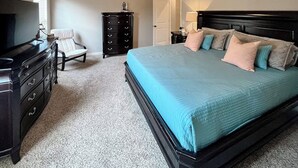 Un dormitorio con cama, cómoda, silla y televisor.