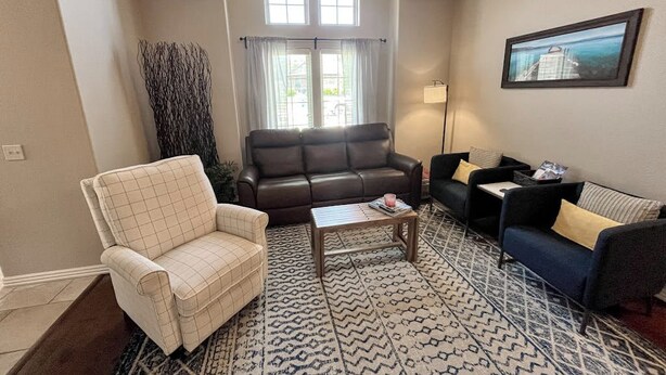 Una sala de estar con un sofá de cuero marrón, un sillón estampado y un sofá azul con cojines amarillos. Hay una alfombra estampada en el suelo, y un cuadro en la pared.