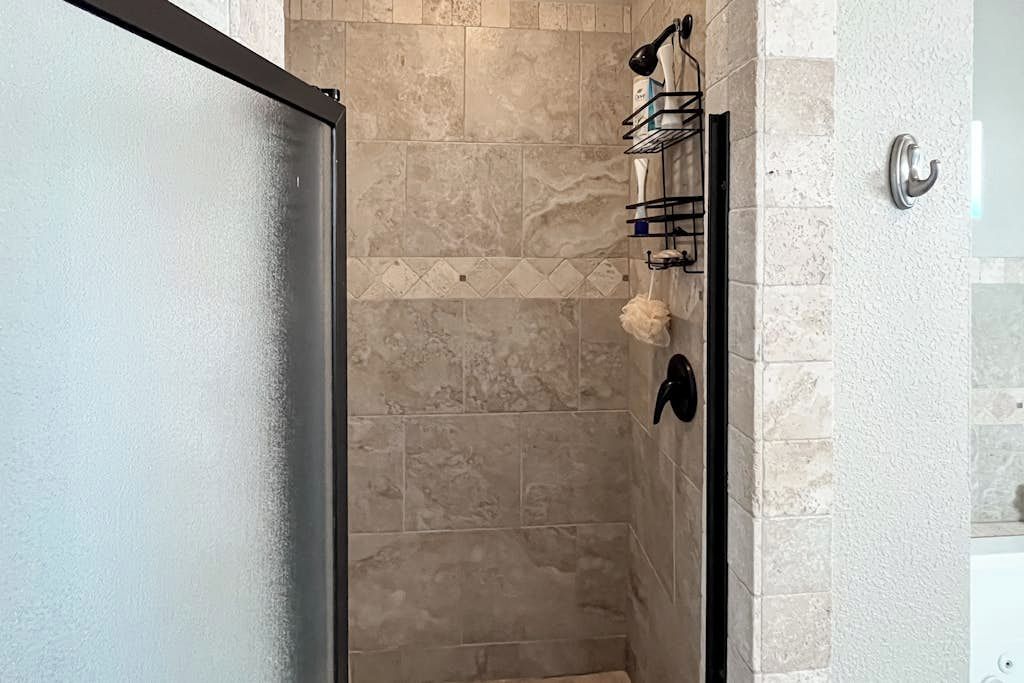 Um banheiro com chuveiro de vidro, azulejos bege, um porta-toalhas e uma toalha.