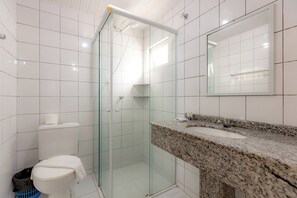 Een badkamer met een douche met glazen wand, een wit toilet, een wastafel met granieten blad en een spiegel boven de wastafel.