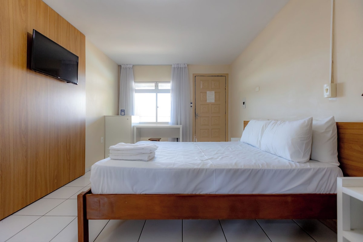 Hotelkamer met een houten bed, een flatscreen televisie aan de muur, een bureau en een raam met gordijnen.