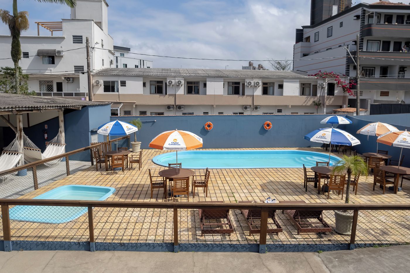 Zona de piscina con sillas de descanso y sombrillas, rodeada por una cerca.