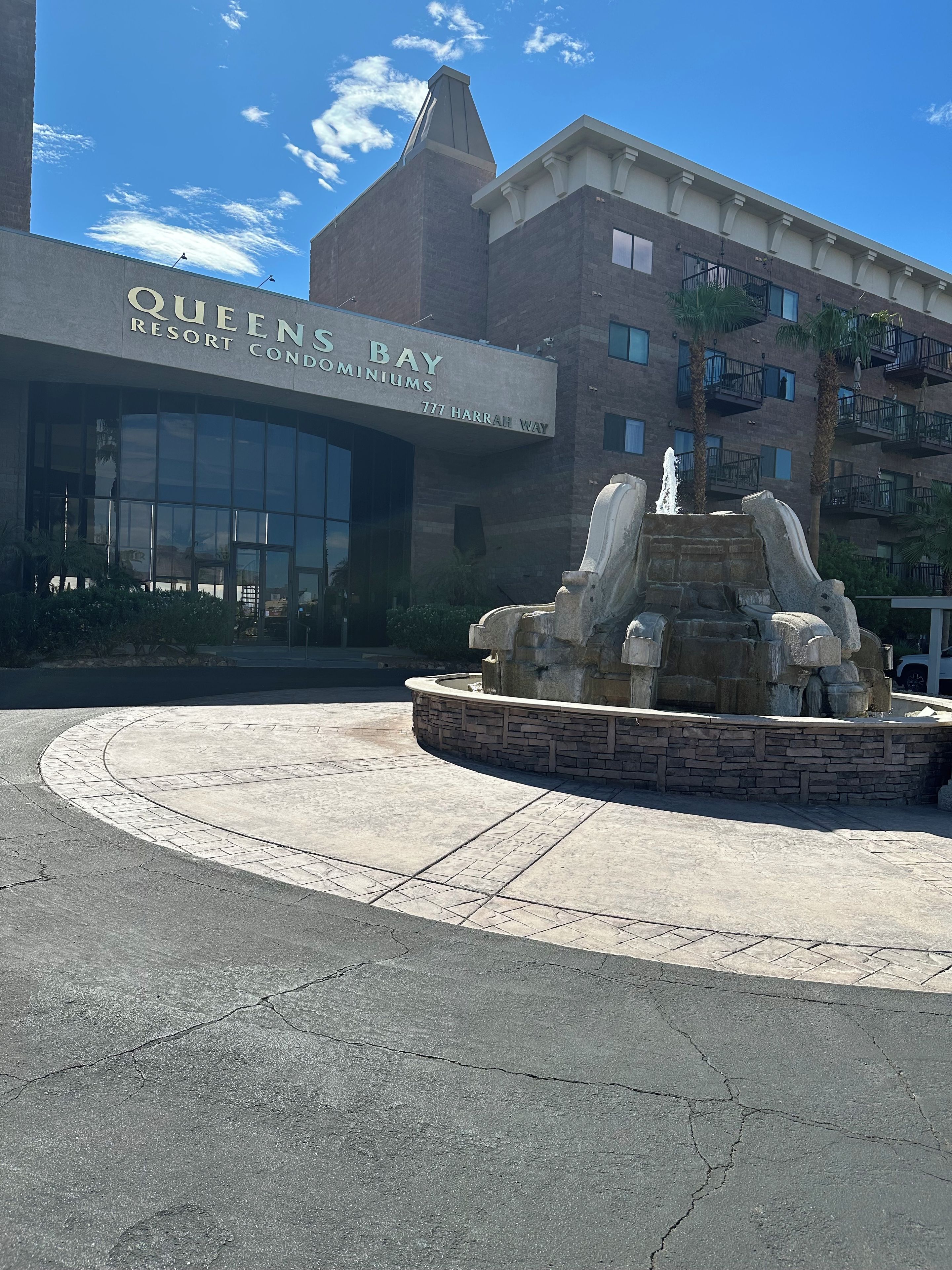Edifício com um letreiro que diz 'Queens Bay Resort Condominiums' e uma fonte em frente.