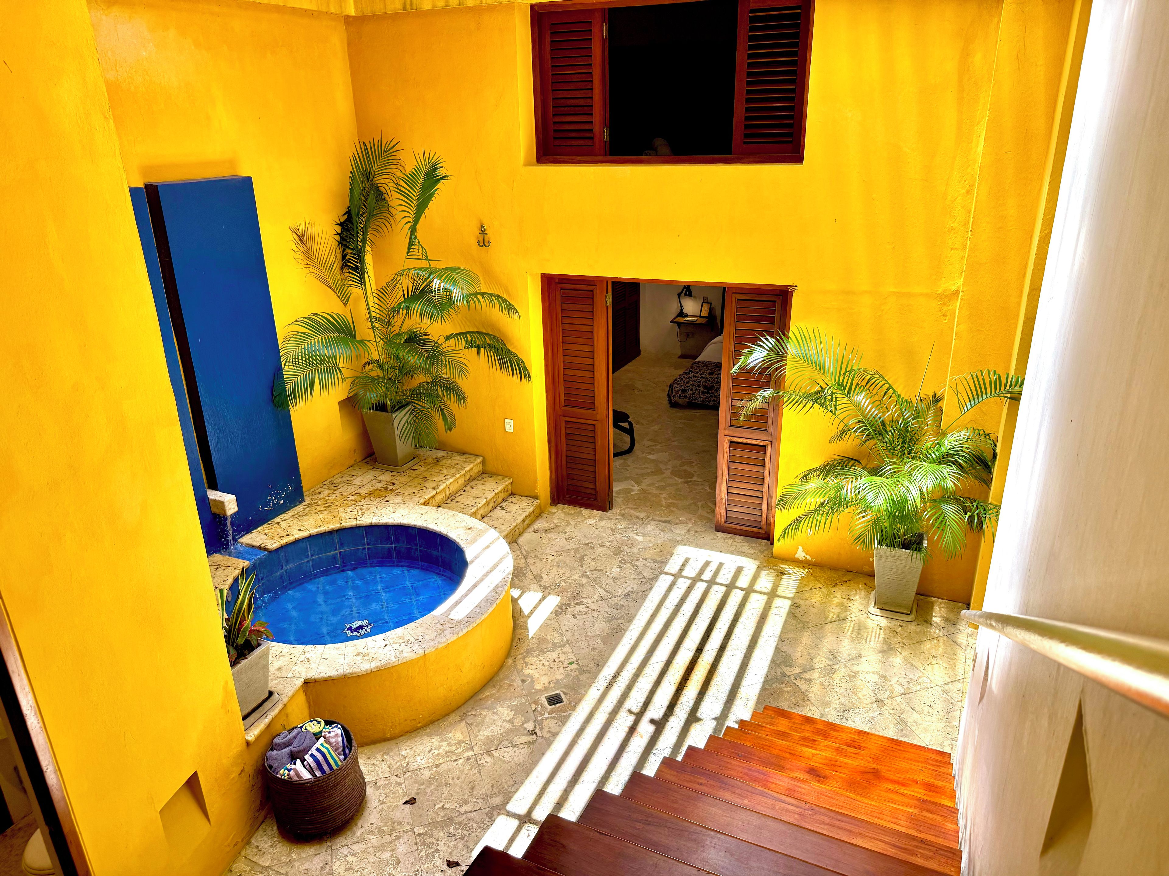A small courtyard with a swimming pool, potted plants, and a wooden staircase.
