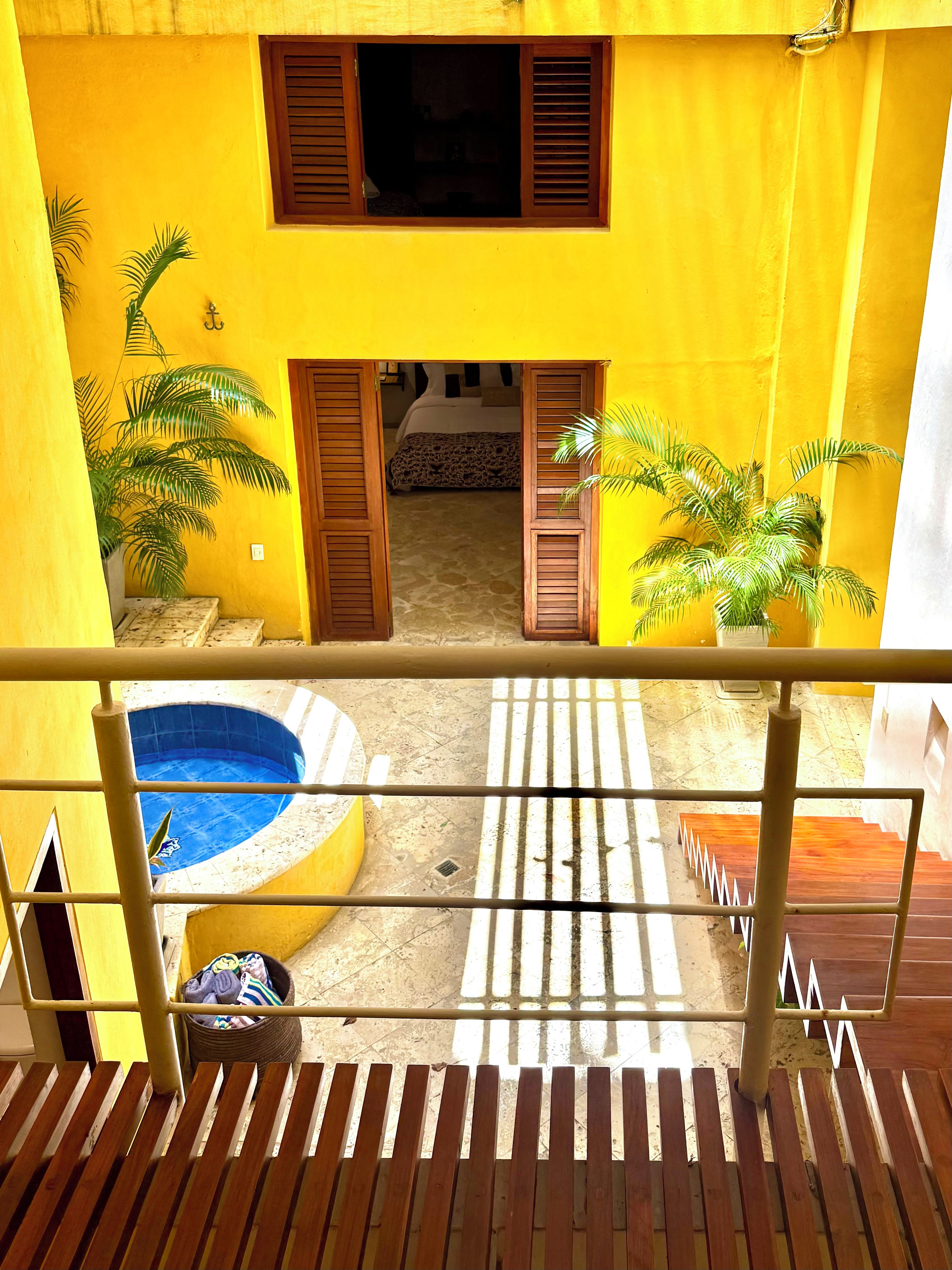 A yellow building with a pool, wooden shutters, and potted plants.