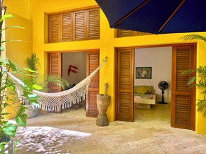 A yellow building with wooden shutters, a hammock, and potted plants. - Calamari Homes - El Porvenir 205 - Walled City (Cartagena de Indias)