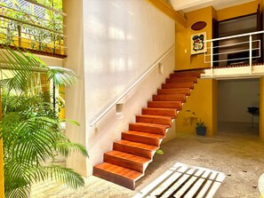 A staircase with wooden steps leading to a balcony, surrounded by potted plants and a tiled floor. - Calamari Homes - El Porvenir 205 - Walled City (Cartagena de Indias)