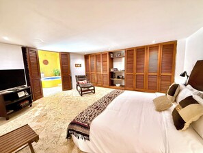 Ein Schlafzimmer mit einem großen Bett, einem Fernseher, einem Sessel und Holzjalousien.